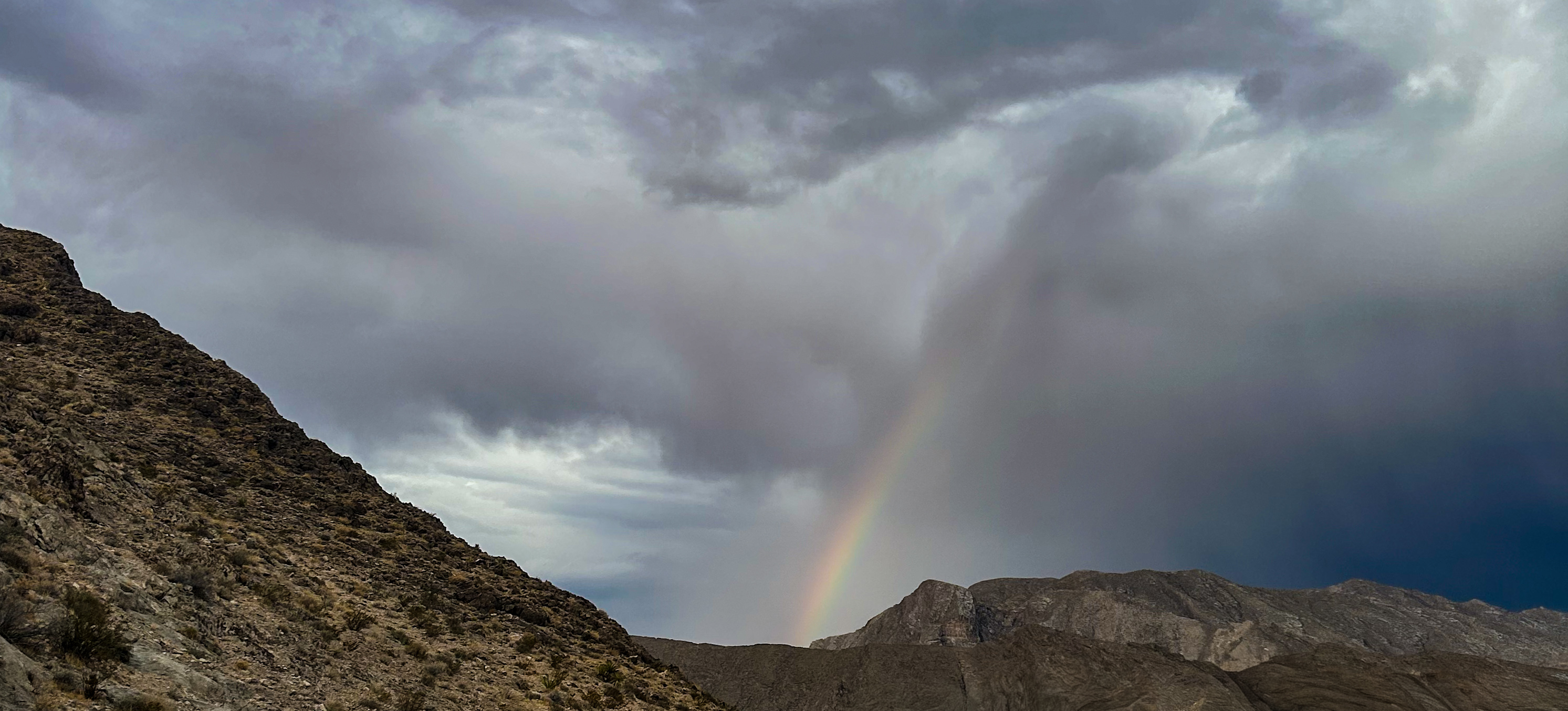 A rainbow behind some mountains in the desert.